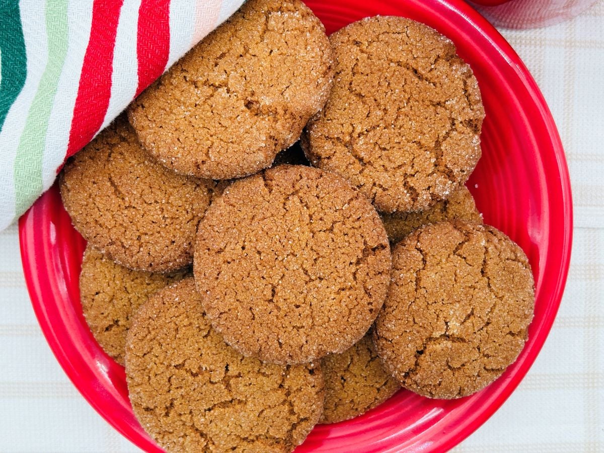 A red plate filled with round, brown cookies, partially covered by a red, green, and white striped cloth.