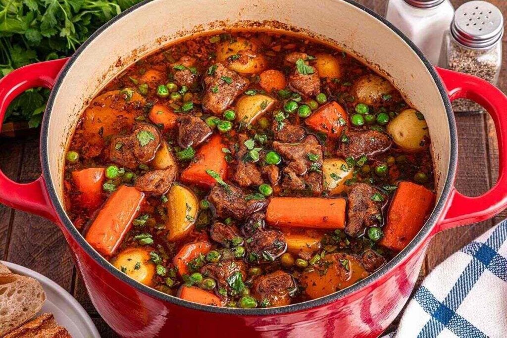 A red Dutch oven filled with beef stew featuring chunks of beef, carrots, potatoes, peas, and herbs in a rich broth—perfect for easy one pot meals.