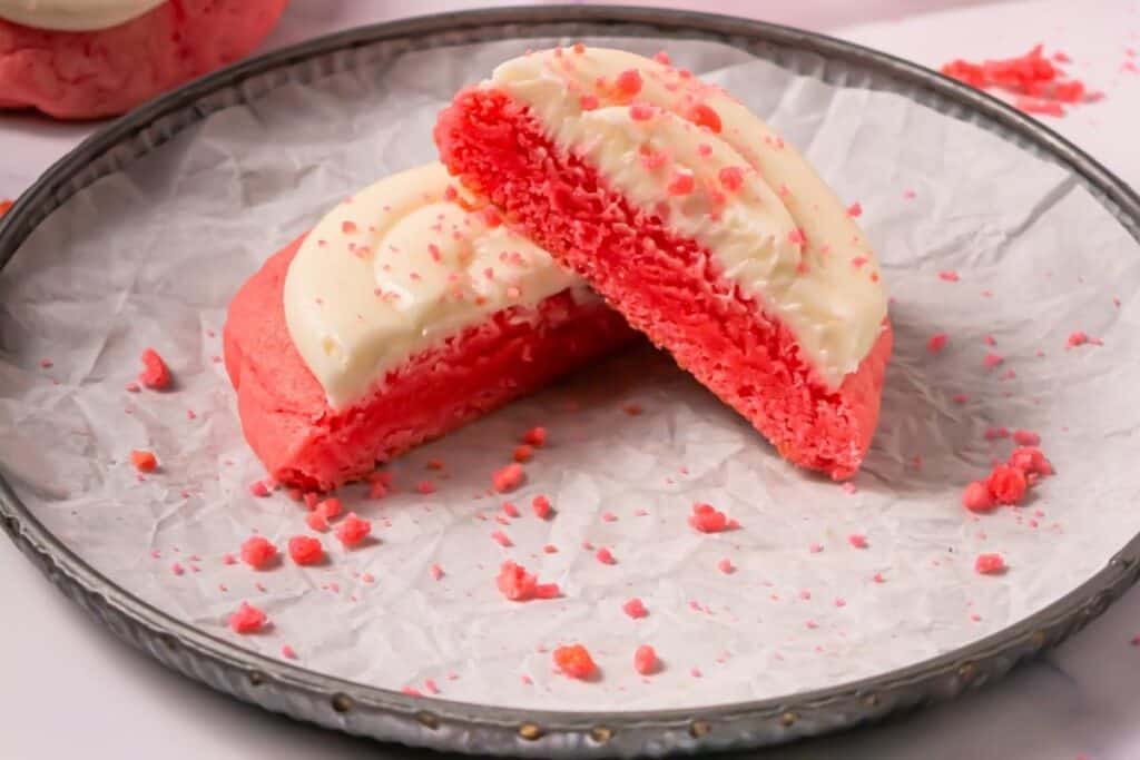 A Crumbl Copycat Pink Velvet Cookies is cut in half and displayed on a round metal tray lined with crinkled parchment paper.