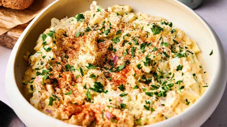 A bowl of creamy egg salad topped with chopped parsley and paprika.