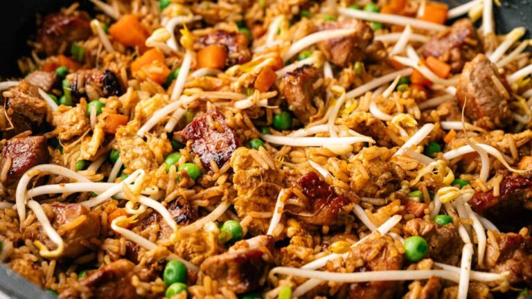 A close-up of stir-fried rice with chunks of meat, peas, carrots, scrambled egg, and bean sprouts mixed together.