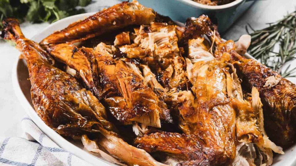 Platter of roasted turkey pieces with crispy brown skin, served on a white dish with a checkered towel visible underneath.