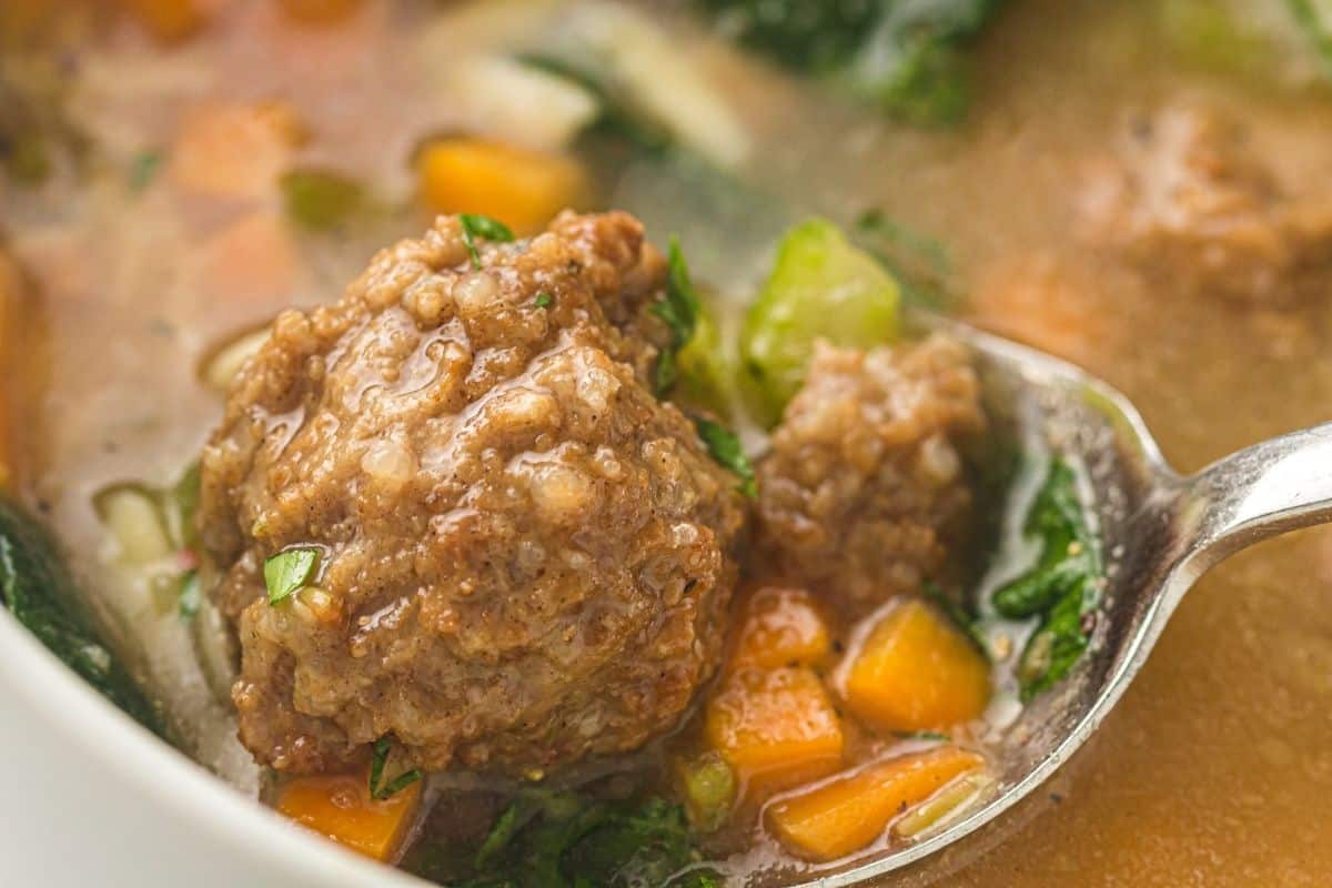 A close-up of a spoon holding a meatball in a bowl of Slow Cooker Italian Wedding Soup.