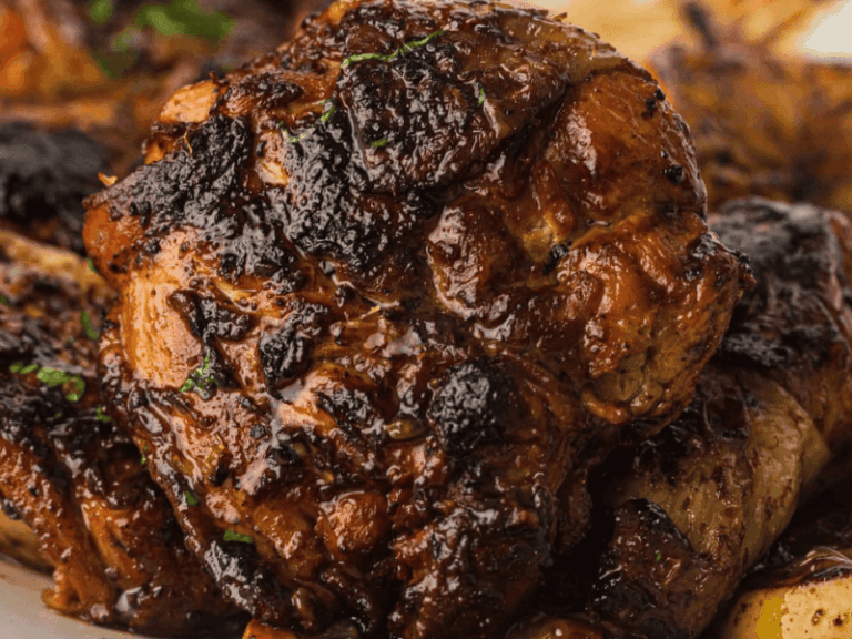 Close-up of a grilled, well-seasoned piece of chicken with a charred exterior, showing grill marks and a glossy, browned surface.