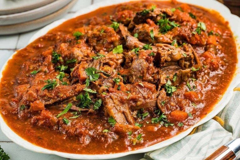A plate of shredded beef in a thick tomato-based sauce, garnished with chopped fresh herbs.