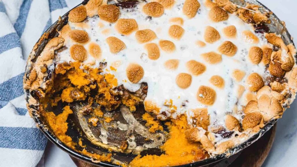 A baked sweet potato casserole topped with toasted marshmallows in a pie dish, with a portion served and a visible interior.