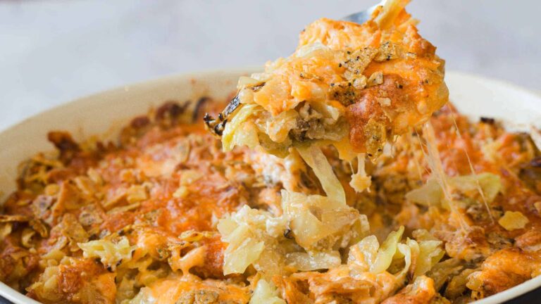 A serving of cheesy, baked casserole with cabbage and a golden, crispy top is being lifted from a white dish.