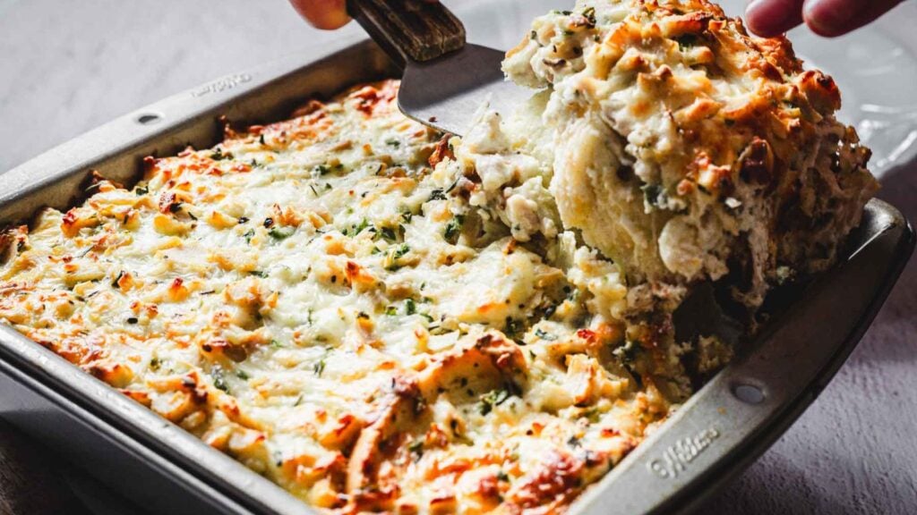 A baked casserole with a golden, cheesy top is being served from a metal pan with a spatula.