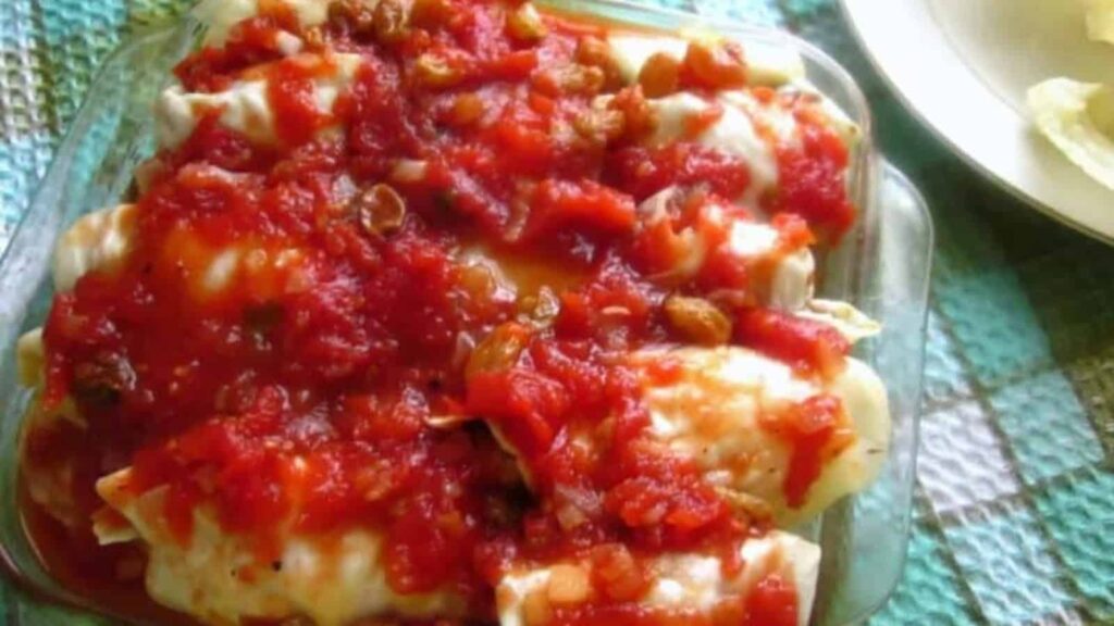 A glass baking dish filled with stuffed cabbage rolls topped with chunky tomato sauce, resting on a checkered cloth.