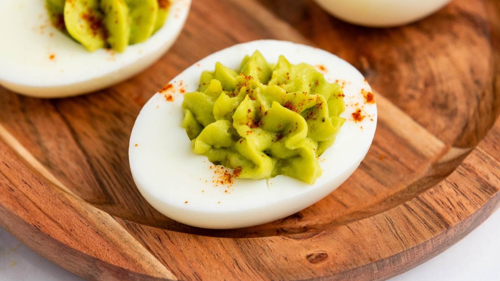 Avocado deviled egg with green filling and a sprinkle of paprika on a wooden plate.