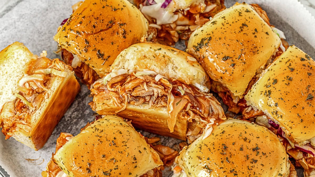 A plate of barbecue chicken sliders with shredded chicken and coleslaw on soft, seasoned buns.