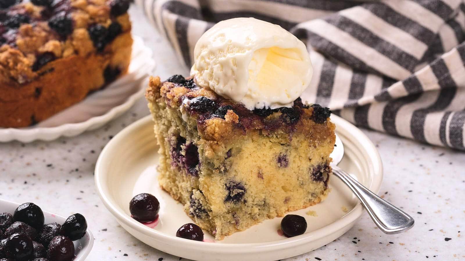 A blueberry buckle topped with a scoop of vanilla ice cream on a plate.