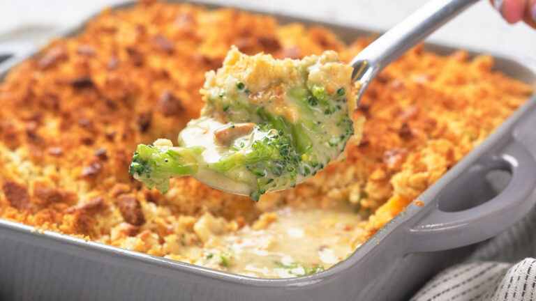 A spoonful of creamy broccoli casserole is lifted from a baking dish with a golden, crumbly topping.