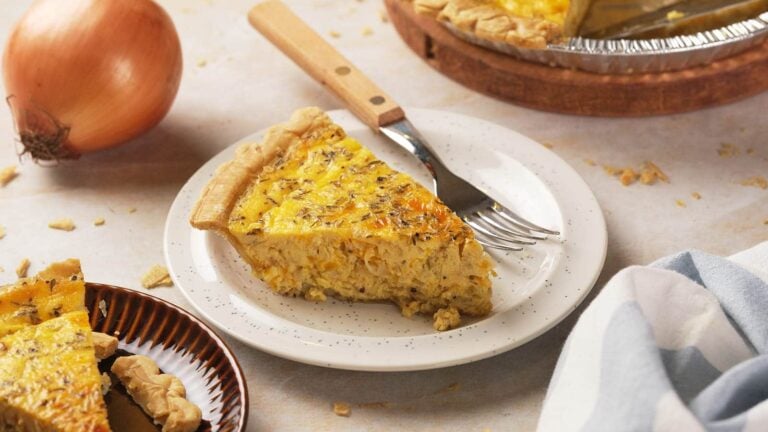 A slice of onion quiche on a white plate with a fork.