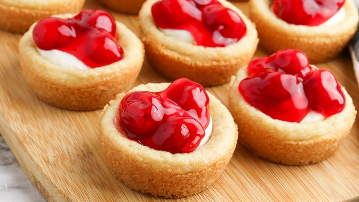 Mini cherry tarts with glossy red cherry topping on a wooden board.