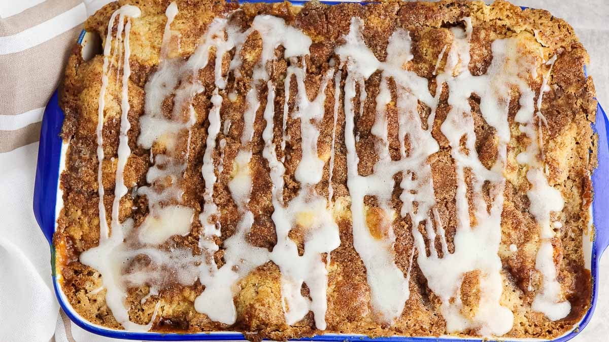 Baked cinnamon roll casserole with icing drizzled on top, served in a blue rectangular dish.