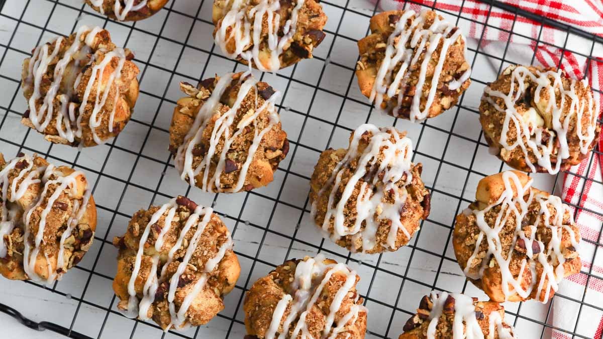 Muffins with crumb topping and icing arranged on a cooling rack with a red and white cloth nearby.