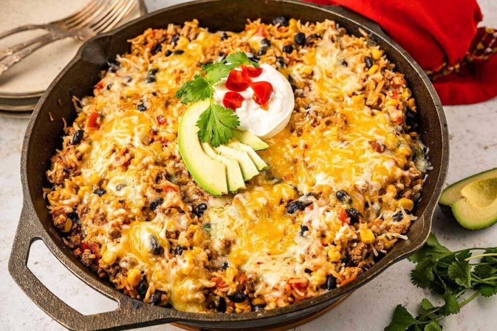 An easy one pot meal, this skillet is filled with cheesy Mexican rice casserole and topped with sliced avocado, sour cream, chopped tomatoes, and cilantro.