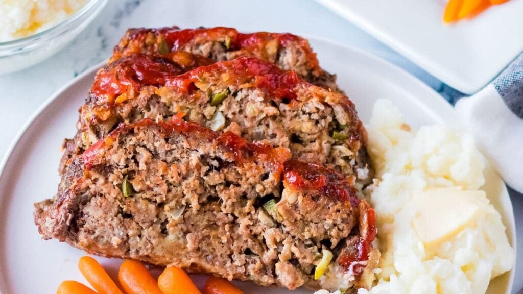 Two slices of meatloaf on a plate with mashed potatoes and carrots.