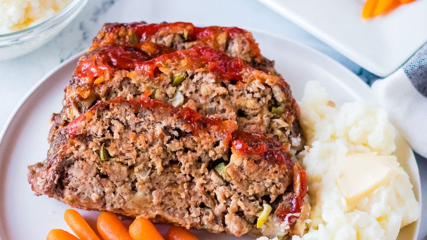 Two slices of meatloaf on a plate with mashed potatoes and carrots.