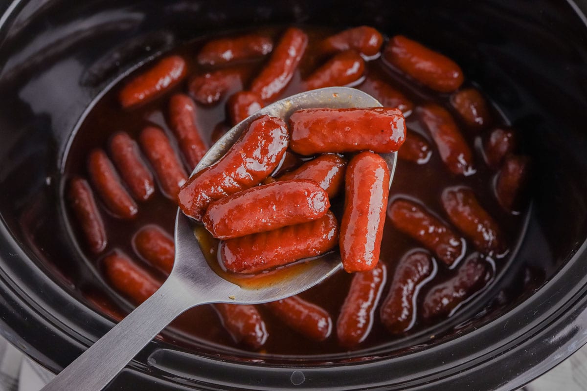Crock pot little smokies on a spoon over the slow cooker.