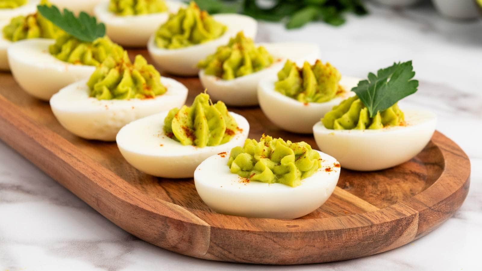 Wooden platter with deviled eggs topped with green filling and a sprinkle of paprika, garnished with parsley.
