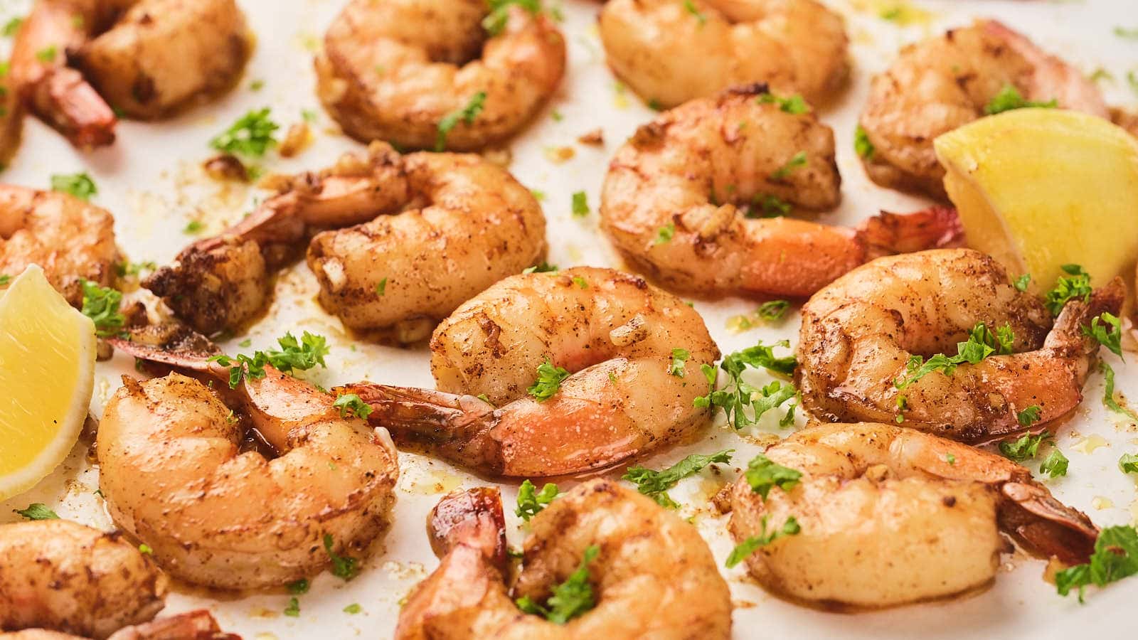 Cooked garlic butter shrimp seasoned with herbs and spices, garnished with chopped parsley, and served with lemon wedges.