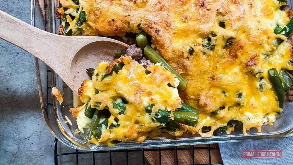 A glass baking dish of cheesy casserole with green beans and ground meat.