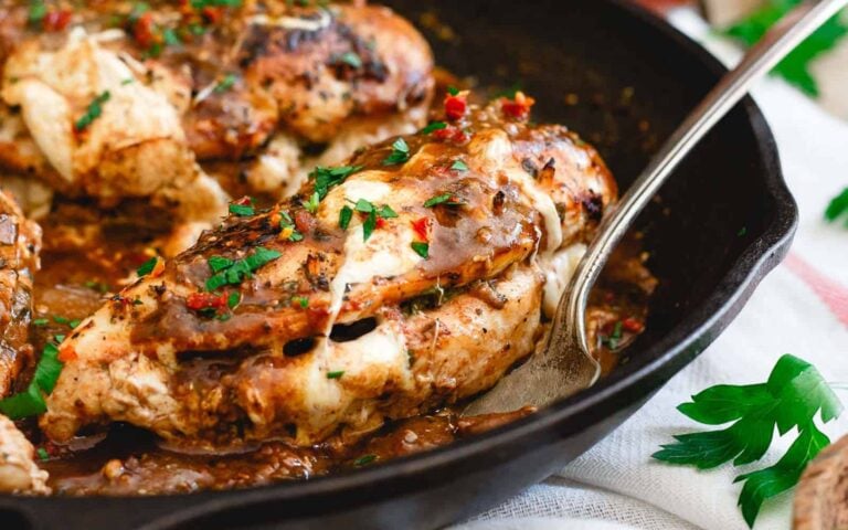 Cooked, seasoned chicken breasts stuffed with melted cheese and herbs, served in a cast iron skillet with a spoon and garnished with fresh parsley.