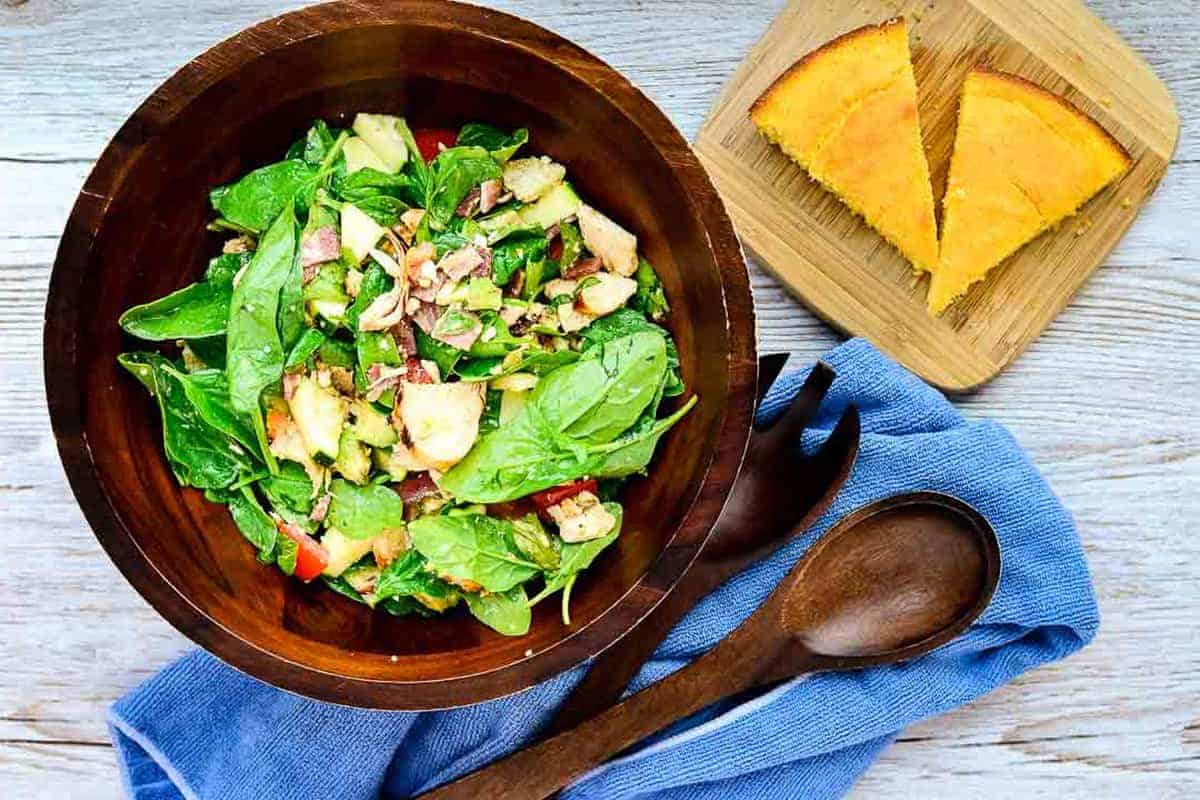 An overhead shot of a wooden serving bowl filled with salad next to cornbread on a cutting board.