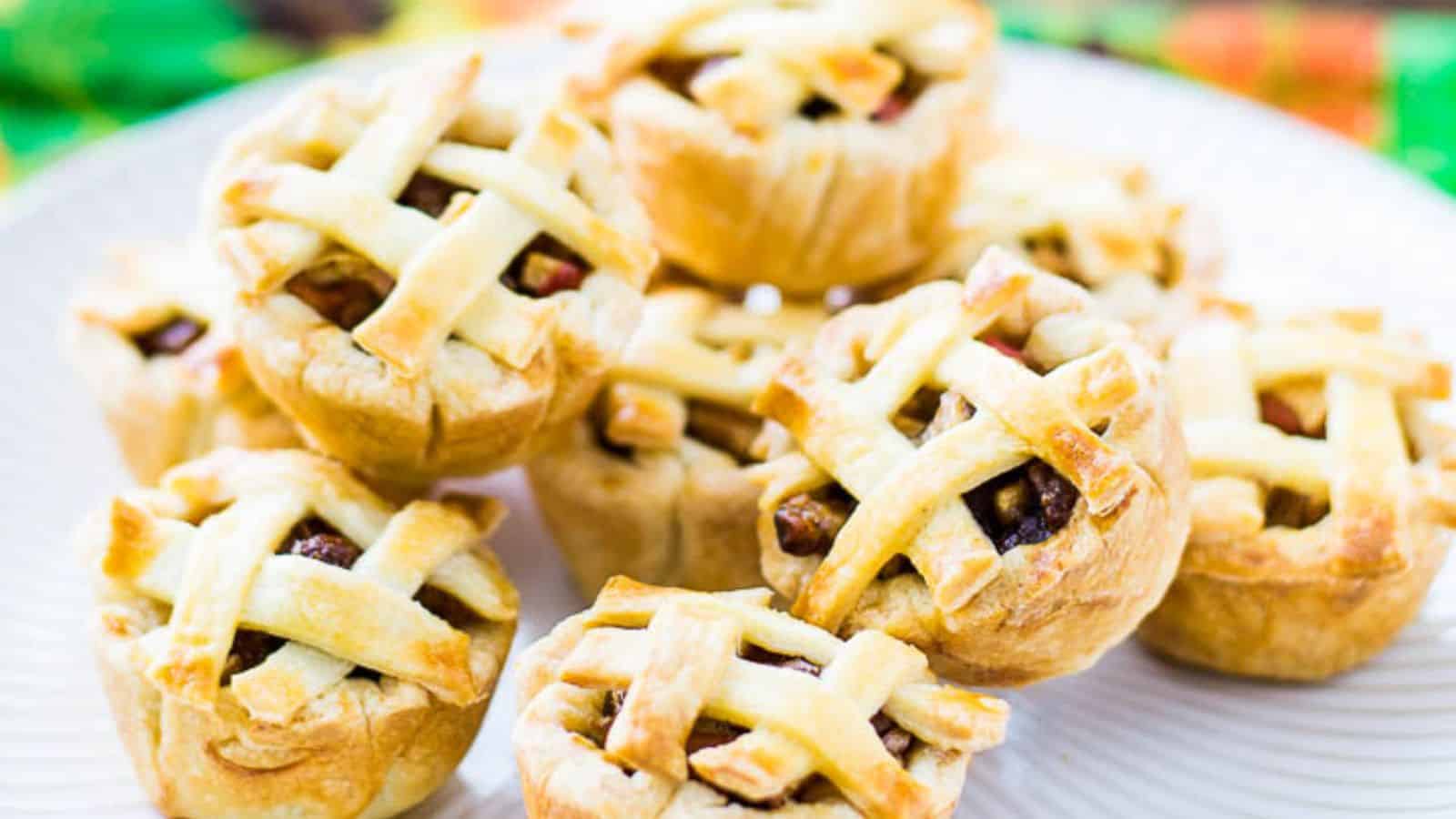 A group of baked mini lattice‑topped apple pies arranged on a baking tin and a plate.