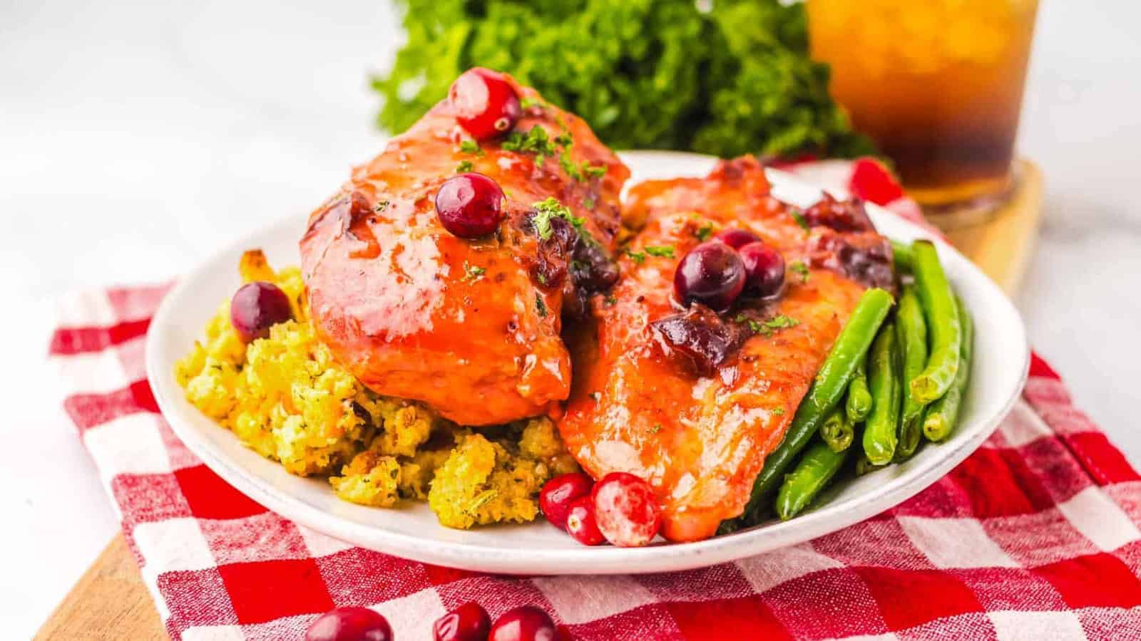Glazed chicken breasts with cranberries, green beans, and stuffing on a white plate, garnished with parsley.