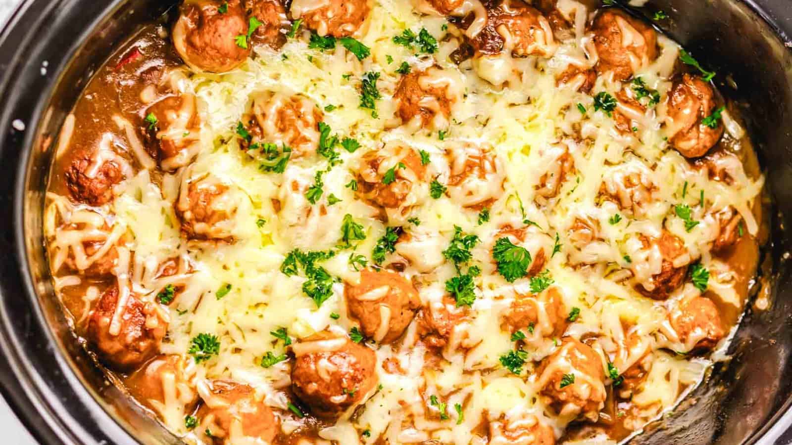 Meatballs topped with melted cheese and chopped parsley in a slow cooker.