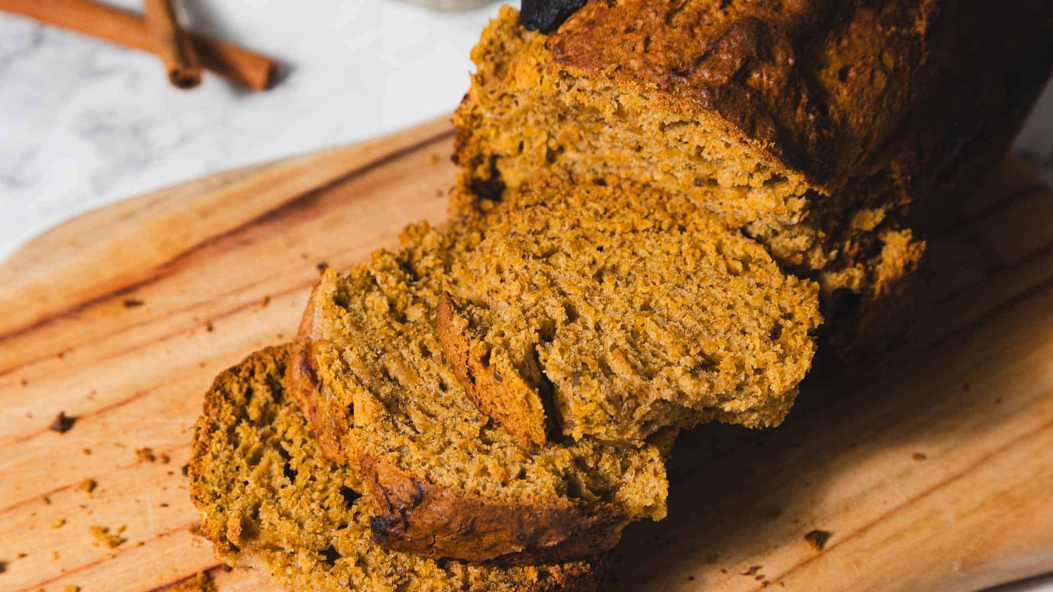 Sliced pumpkin bread on a wooden cutting board next to a glass of milk.