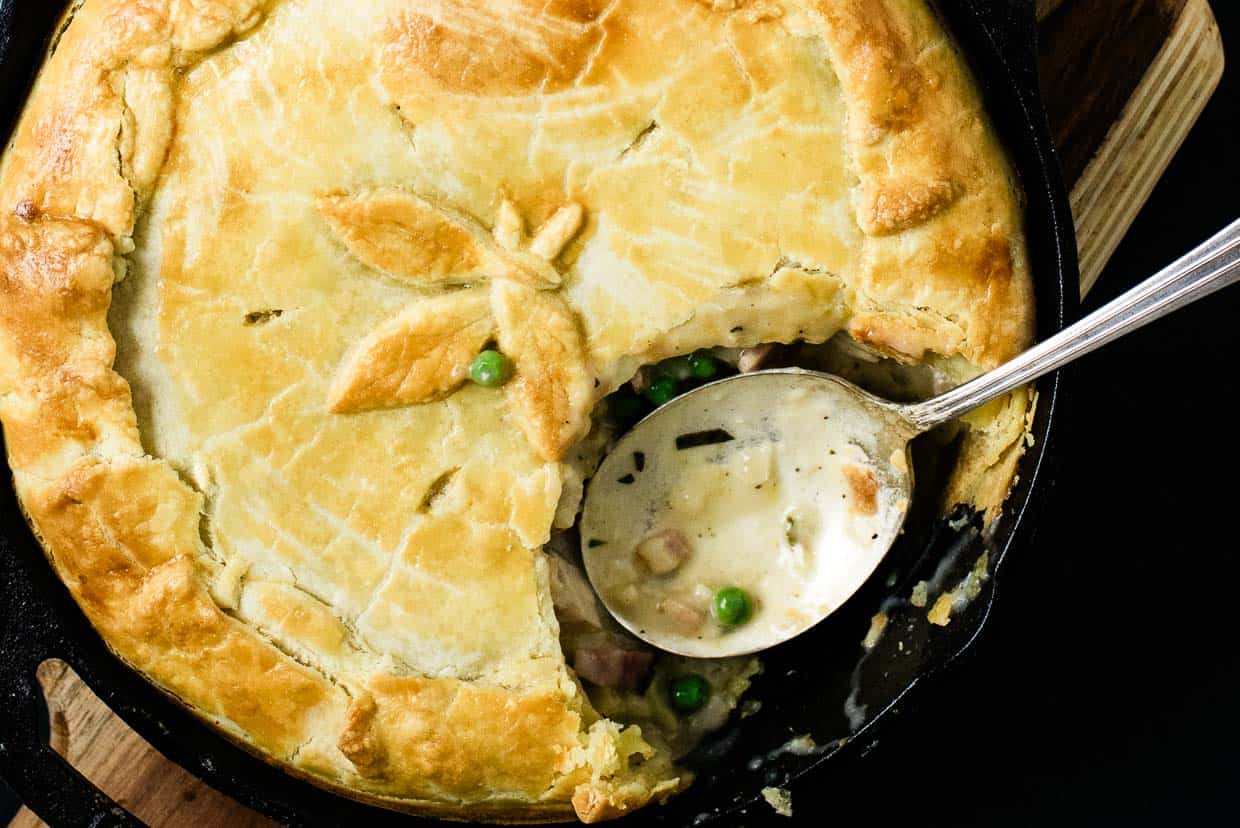 A chicken pot pie in a skillet with a silver spoon rests inside.