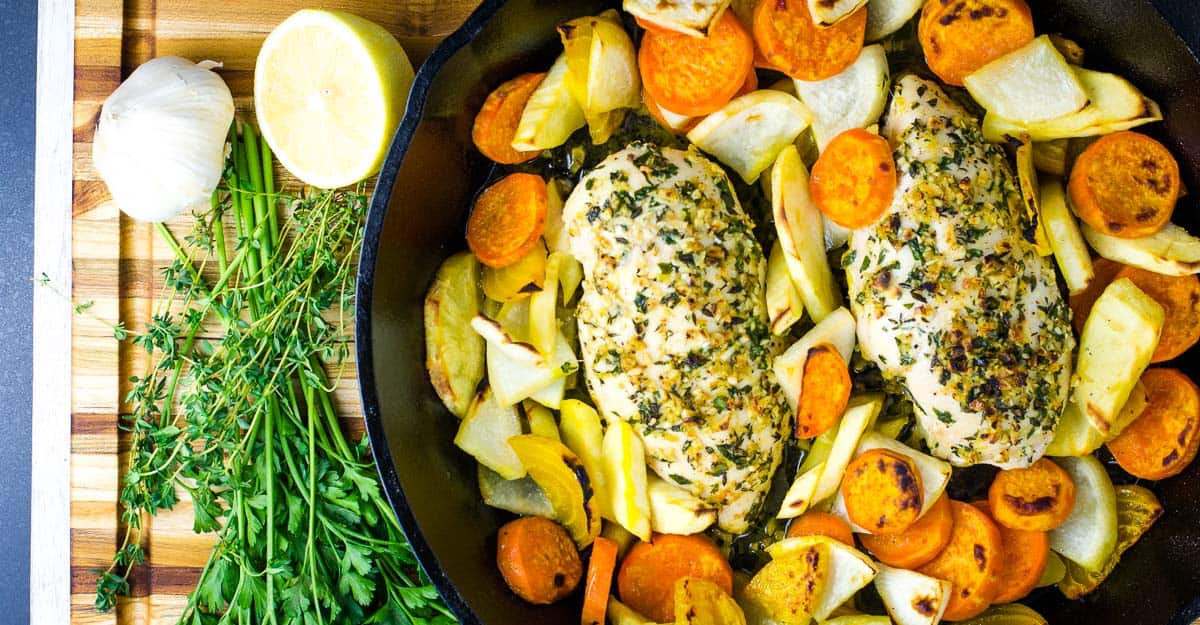 Roasted chicken and vegetables in a skillet on a cutting board.