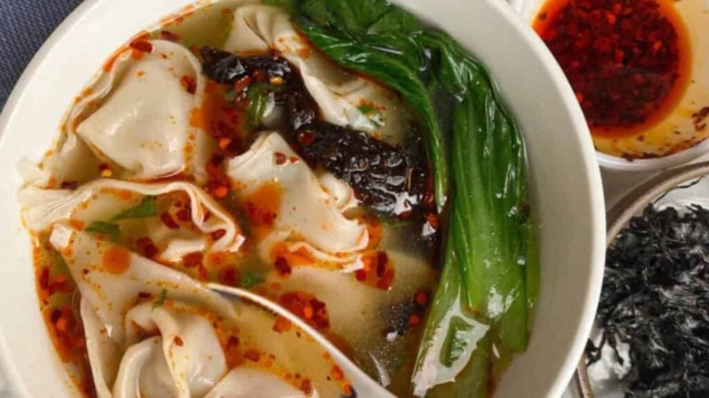 Bowl of wonton soup with broth, green vegetables, seaweed, and chili oil.