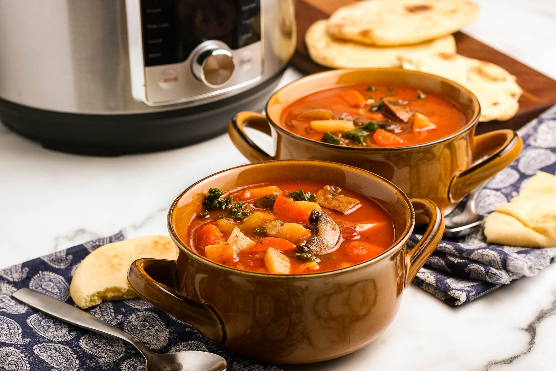 Two bowls of instant pot vegetable soup in front of the pressure cooker.