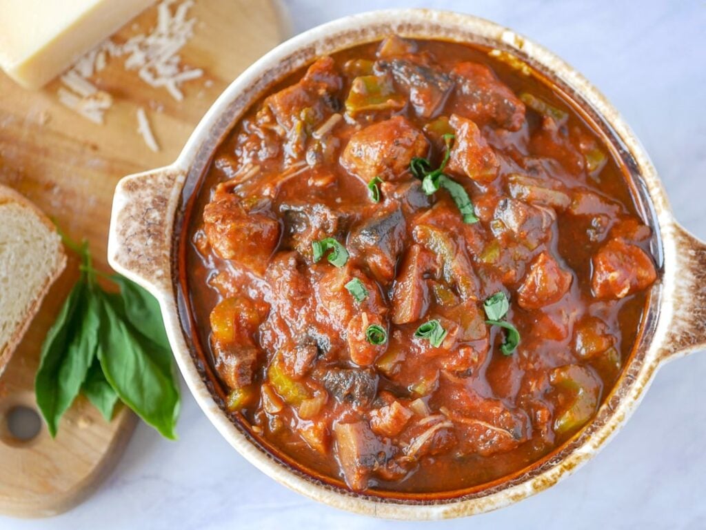 Top view of a big pot of mushroom stew with cheese and basil on a cutting board next to the pot.