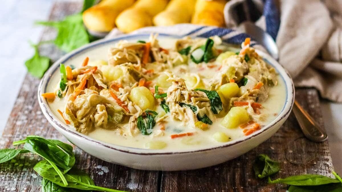 Bowl of copycat Olive Garden chicken gnocchi soup in a bowl with breadsticks in the background.