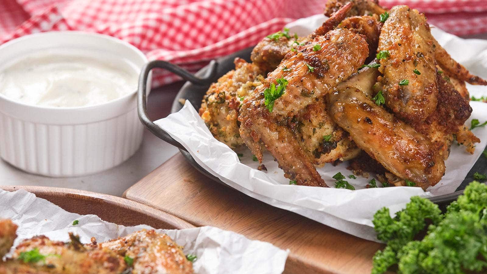 A plate of parmesan and garlic wings garnished with herbs is served on parchment paper.