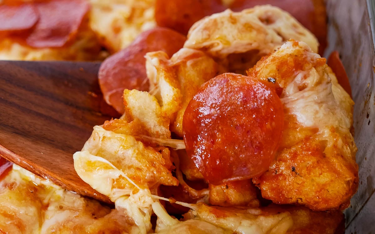 Close-up of pizza with pepperoni and melted cheese being served with a wooden spatula.