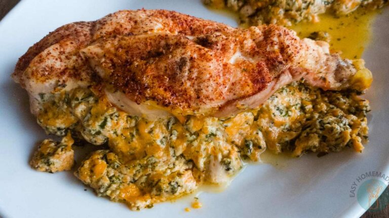 A cooked, seasoned chicken breast sits on a plate, stuffed with a creamy mixture of cheese and herbs.