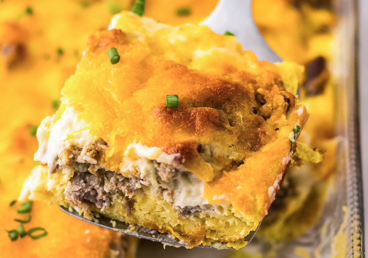 A plate of biscuits covered in creamy sausage gravy sits on a table, accompanied by a halved orange and a yellow mug in the background.