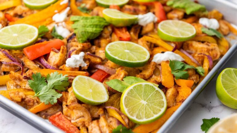 Sheet pan fajitas with sliced chicken, bell peppers, red onions, lime wedges, and fresh cilantro.