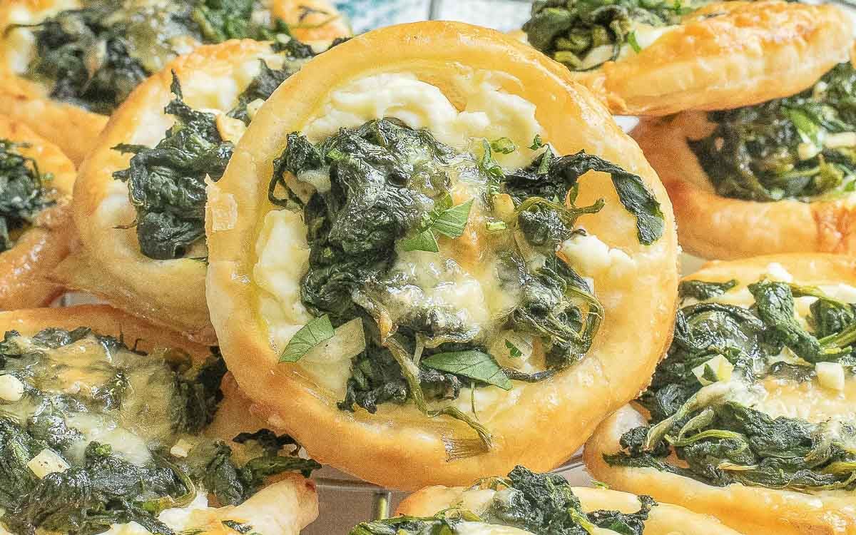 Close-up of pastries topped with spinach and cheese, displayed in a pile.