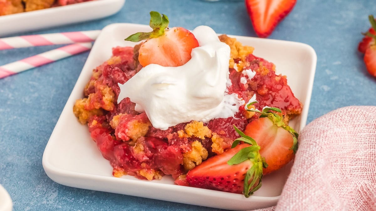 Strawberry dump cake on a plate with whipped cream.