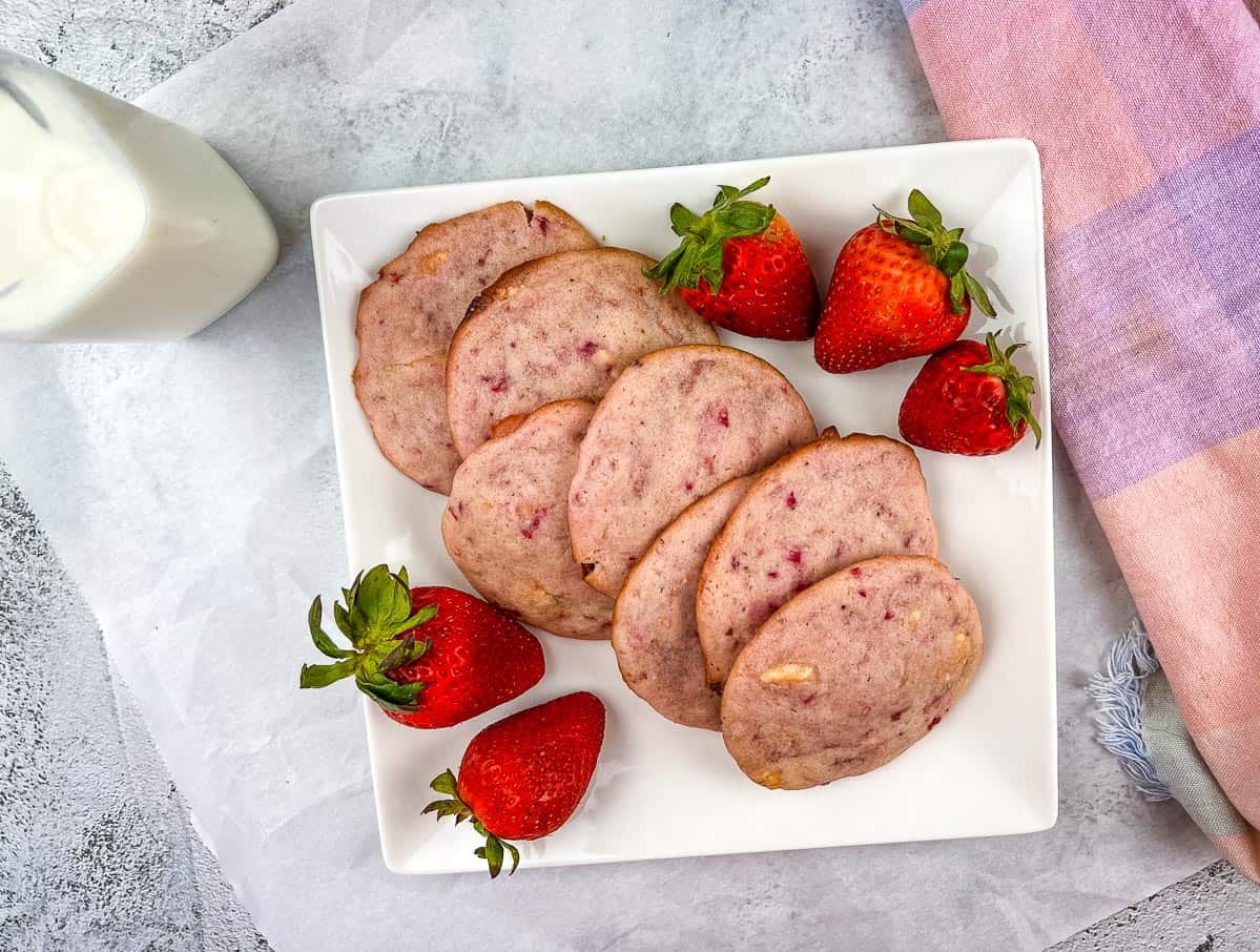 Strawberry Shortcake Cookies on a white plate with strawberries nearby.