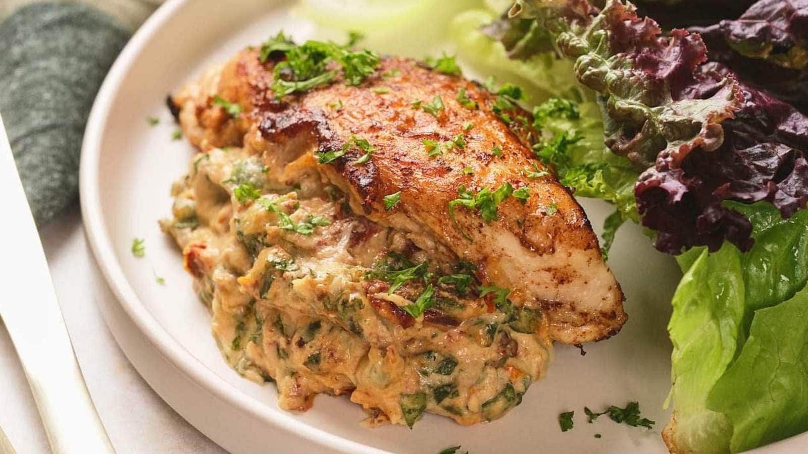 A plate of stuffed chicken breast garnished with chopped herbs and served with fresh leafy greens.