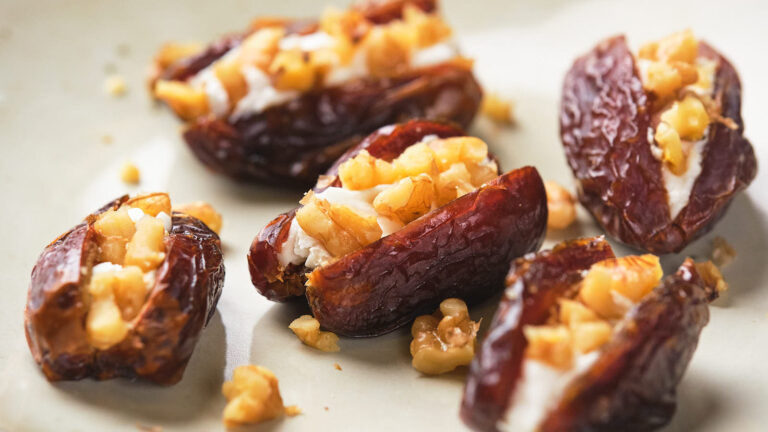 Close-up of dates stuffed with cream cheese and chopped walnuts on a beige plate.